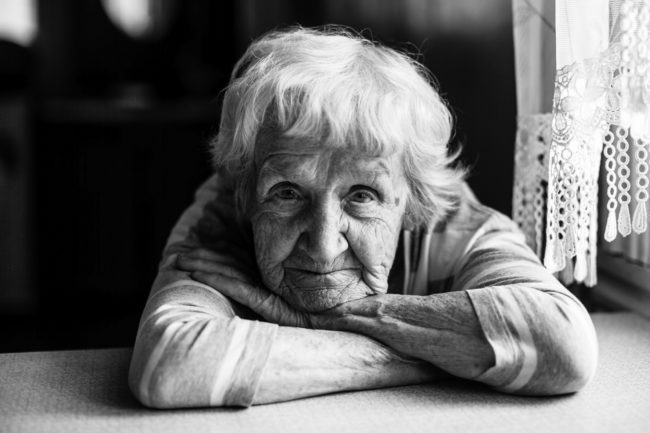 Close-up black and white portrait of a old woman at the table in home.
