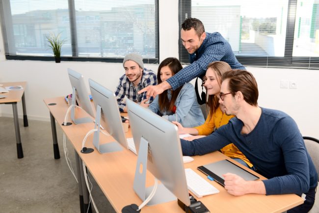 group of five young people student with teacher in photography school learning photo editing with desktop computer, camera and photo equipment