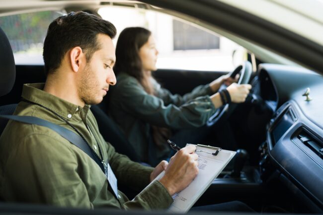 Latin male instructor rating the driving skills of a teen girl