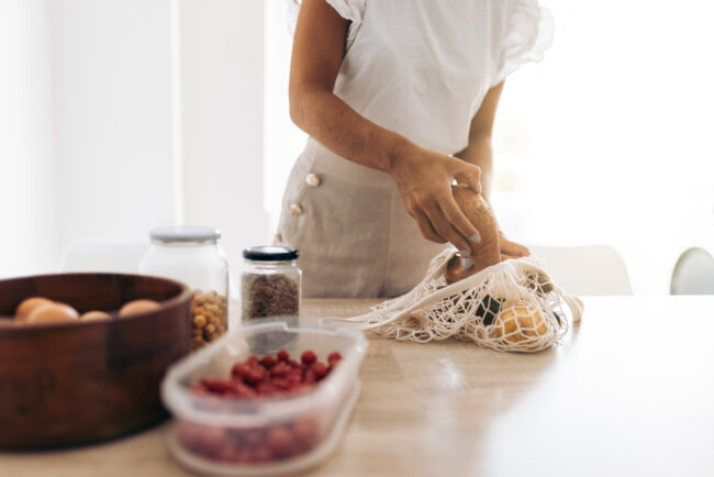 Anonymous crop woman taking vegetables out of a clothing bag