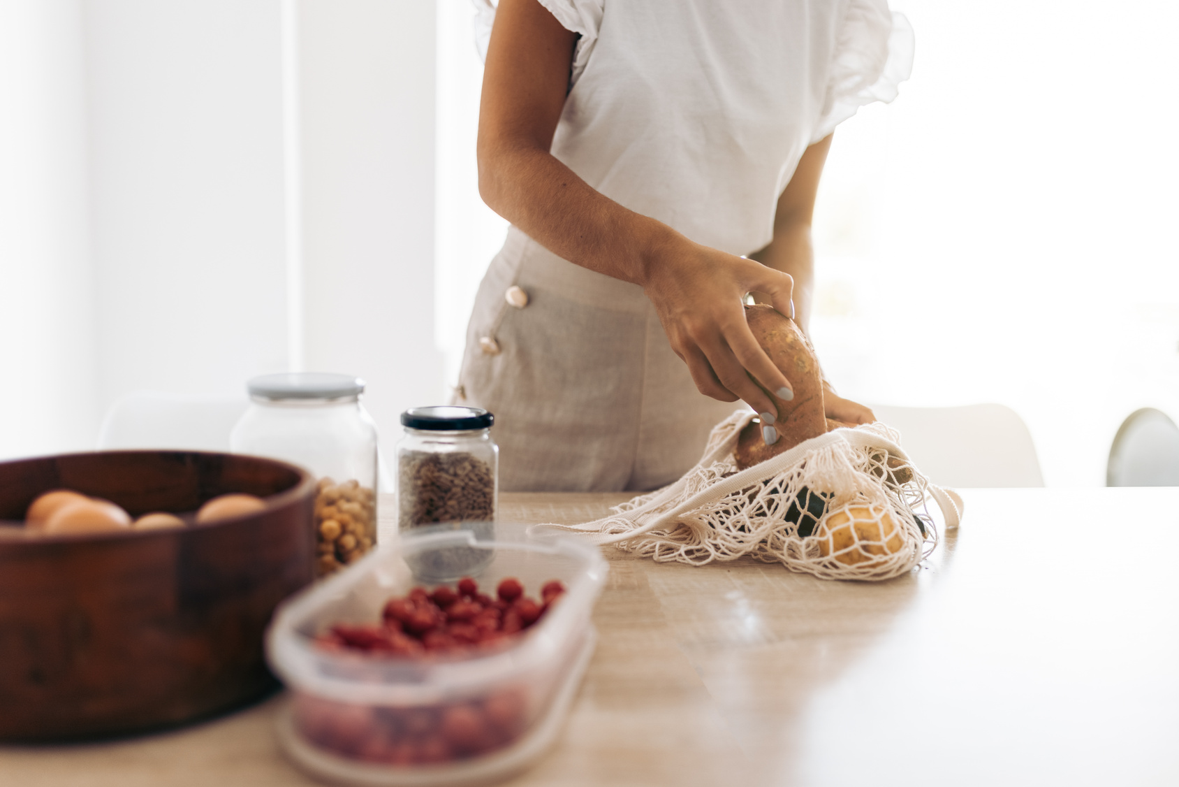 Anonymous crop woman taking vegetables out of a clothing bag